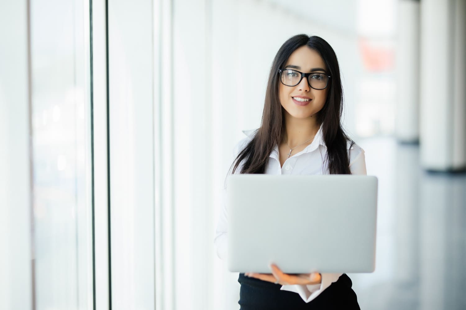 mujer-negocios-joven-que-trabaja-su-oficina-lujo-sosteniendo-computadora-portatil-pie-contra-ventana-panoramica-vistas-al-distrito-negocios (1)